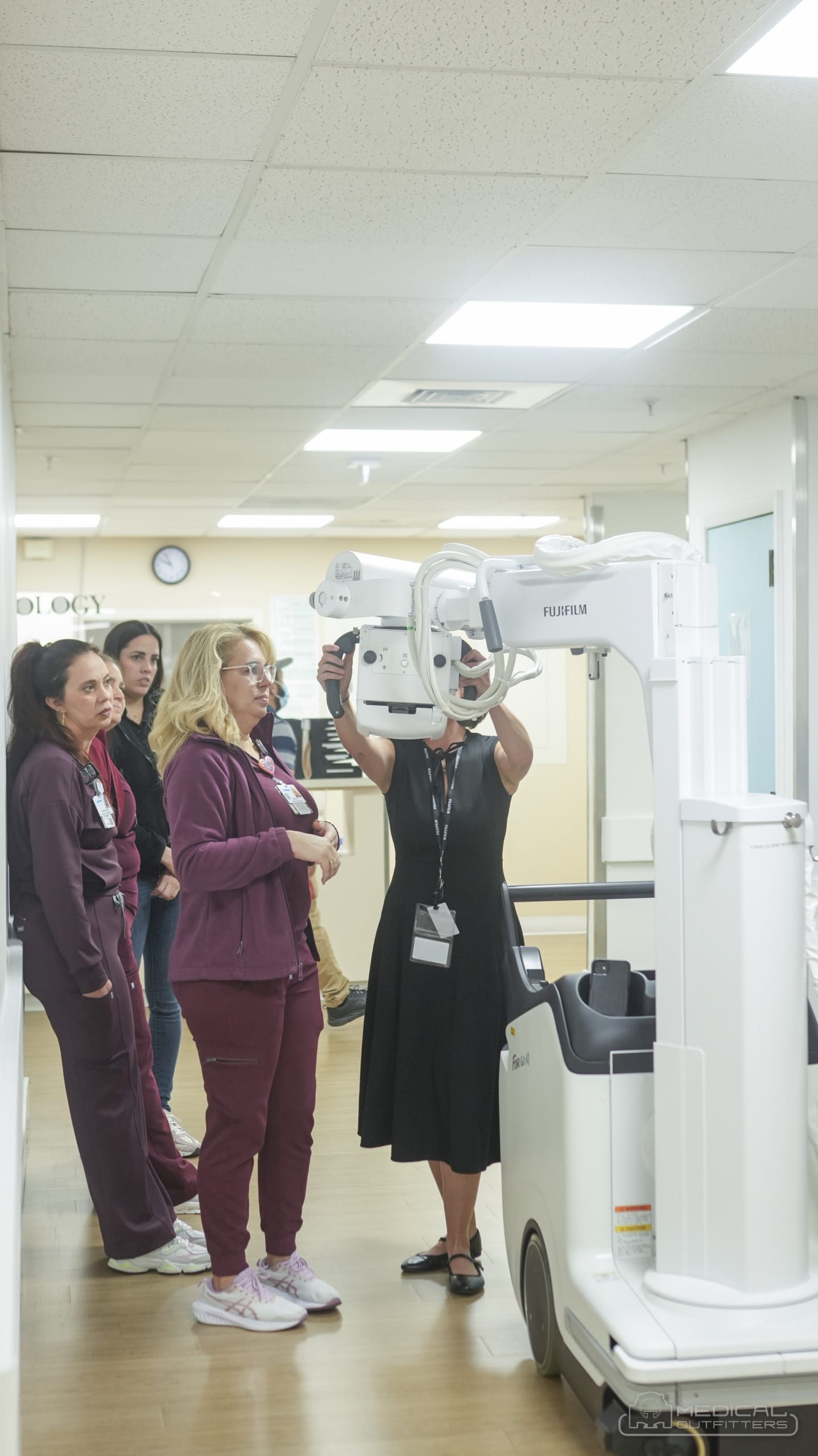 Demonstrator positioning the tube head of the FDR Go iQ mobile X-ray machine while Larkin Community Hospital technologists watch in a corridor