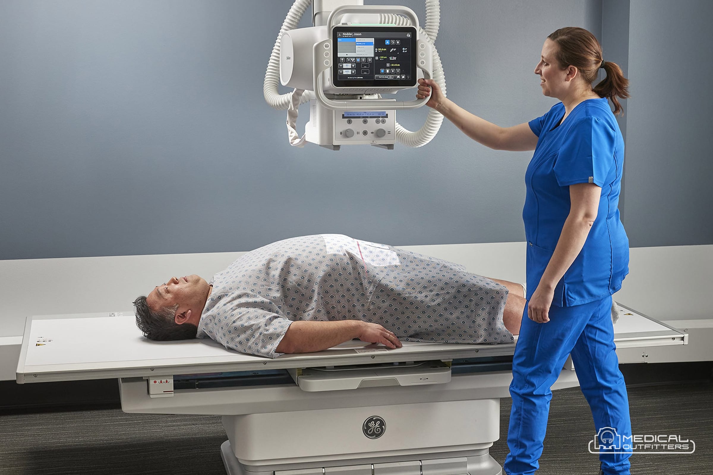 GE Definium X-Ray: Definium 656 HD room with the overhead tube suspension, the table and a technologist positioning a patient, photo courtesy of GE HealthCare