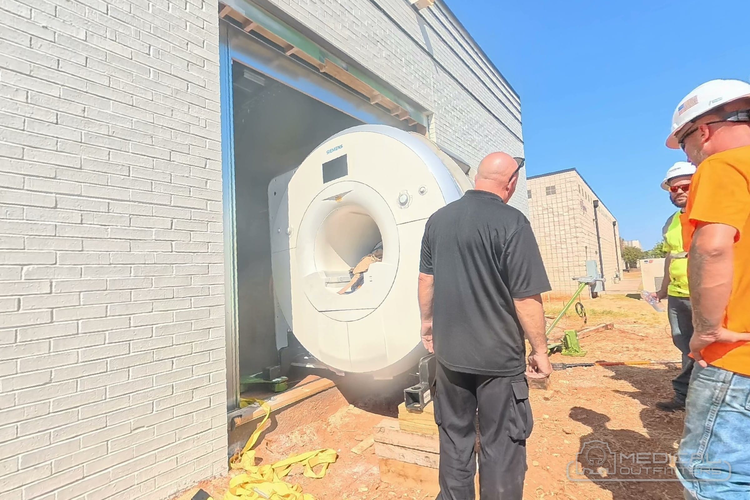 Medical Outfitters delivery crew in hard hats with an MRI magnet at the wall opening of a new magnet room in Oklahoma City
