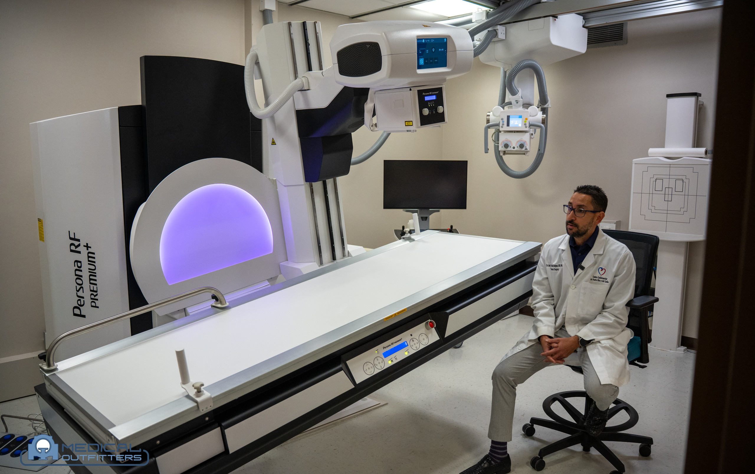 Member of the Centro Cardiovascular de Puerto Rico y del Caribe imaging team seated beside the Fujifilm Persona RF PREMIUM+ table in the new fluoroscopy room