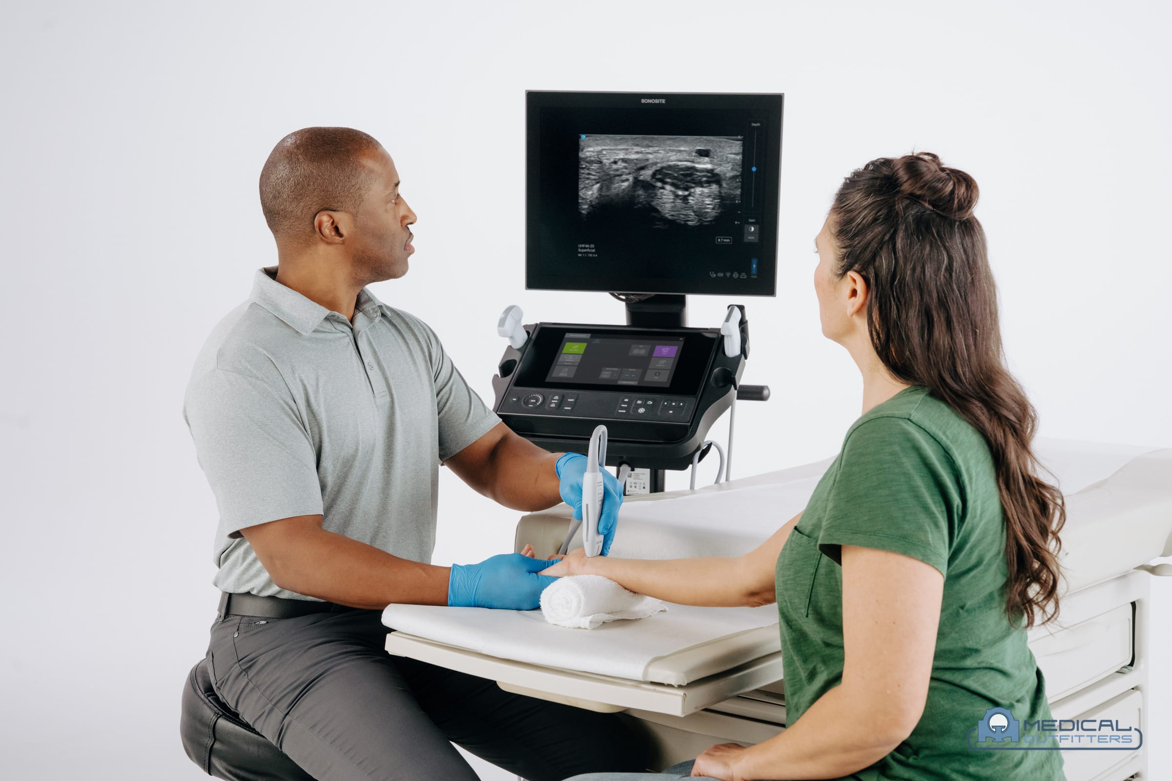 Clinician scanning a patient's wrist with a Fujifilm Sonosite cart-based ultrasound system in a clinic, photo courtesy of Fujifilm Sonosite, with the Medical Outfitters watermark