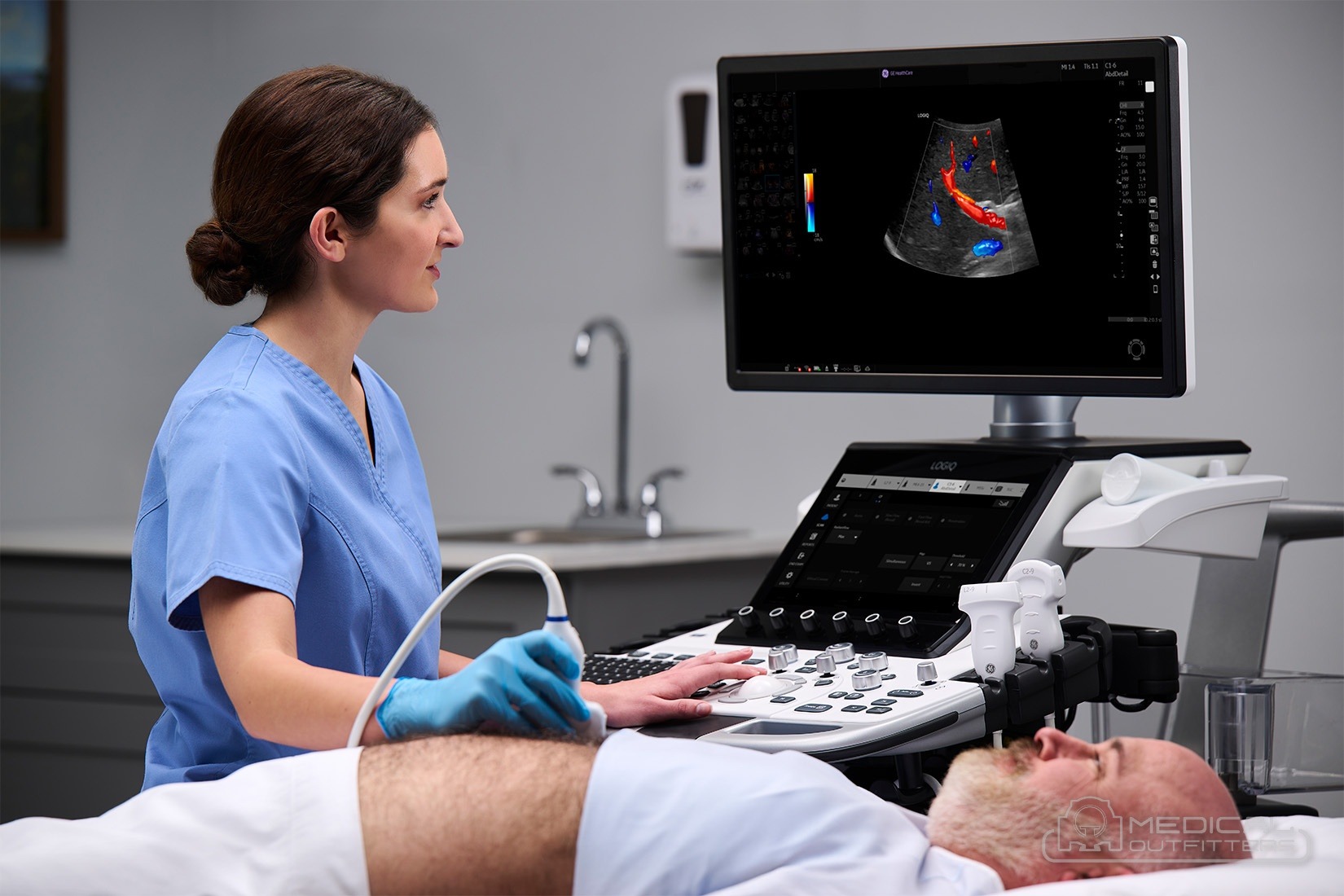 Sonographer scanning a patient's abdomen at a GE HealthCare LOGIQ E10 ultrasound cart, photo courtesy of GE HealthCare, with the Medical Outfitters watermark