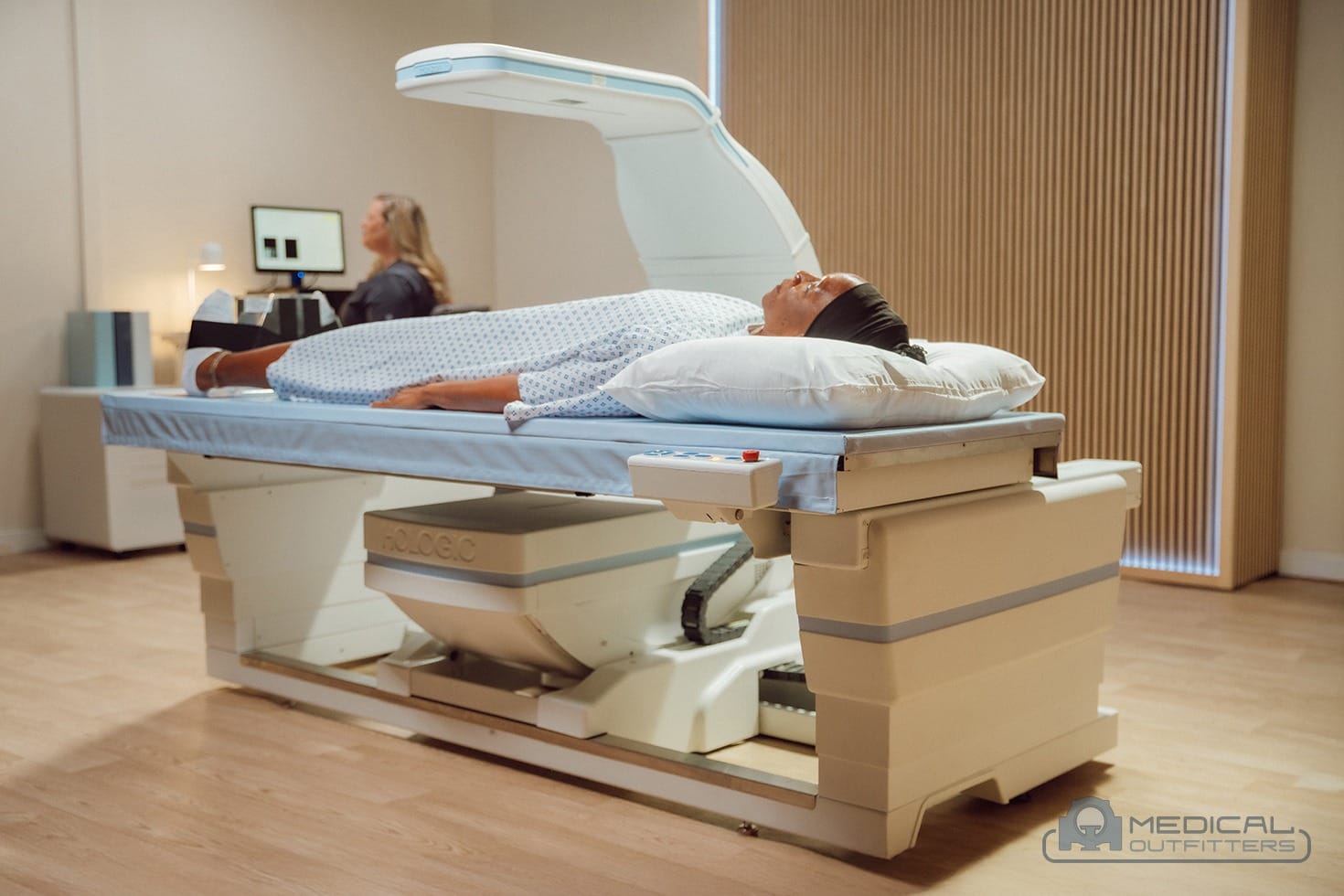 Patient on a Hologic Horizon DXA bone densitometer with the technologist at the console, photo courtesy of Hologic, with the Medical Outfitters watermark