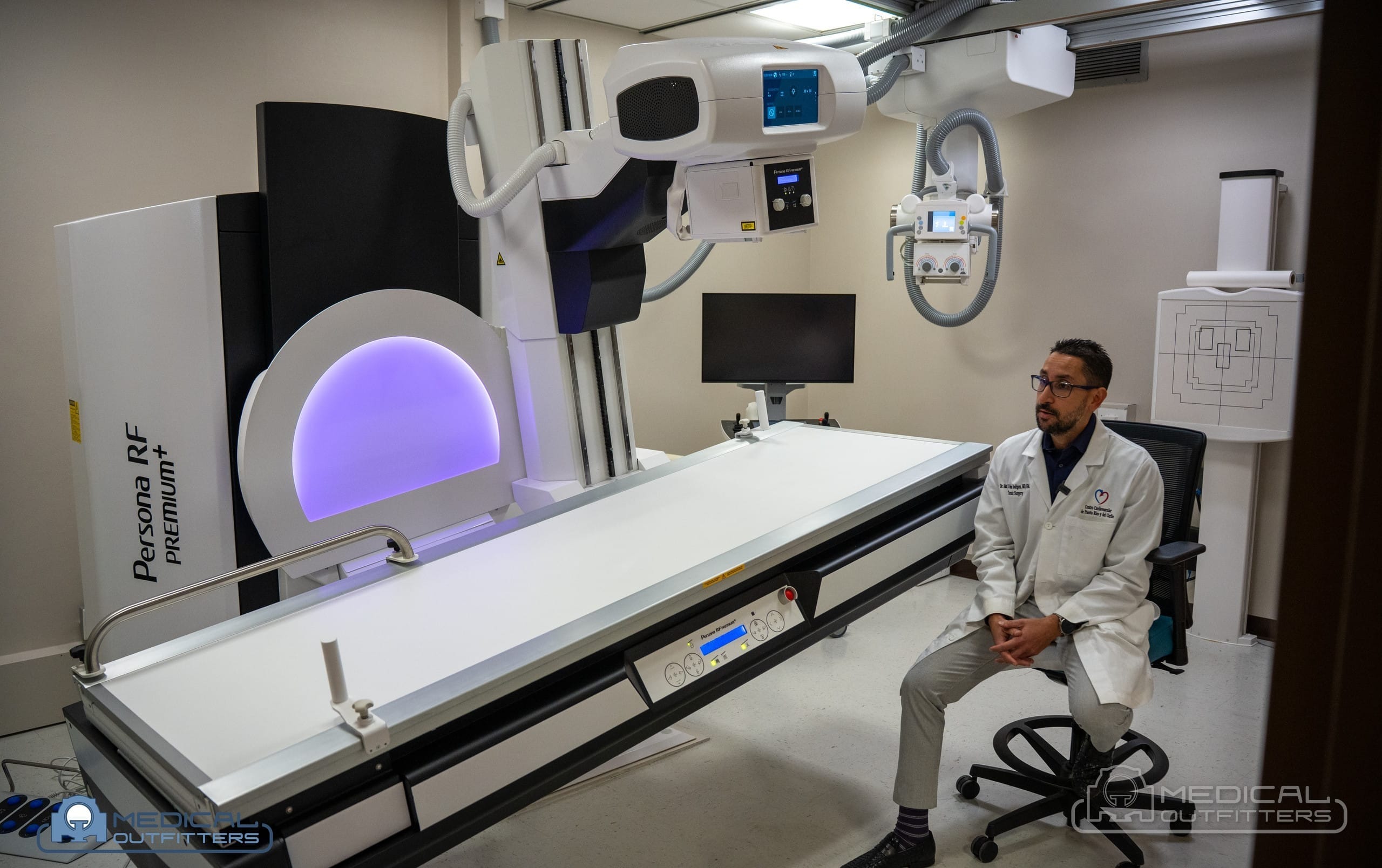 Member of the Centro Cardiovascular de Puerto Rico y del Caribe imaging team seated beside the Fujifilm Persona RF PREMIUM+ table in the new fluoroscopy room, with the Medical Outfitters watermark
