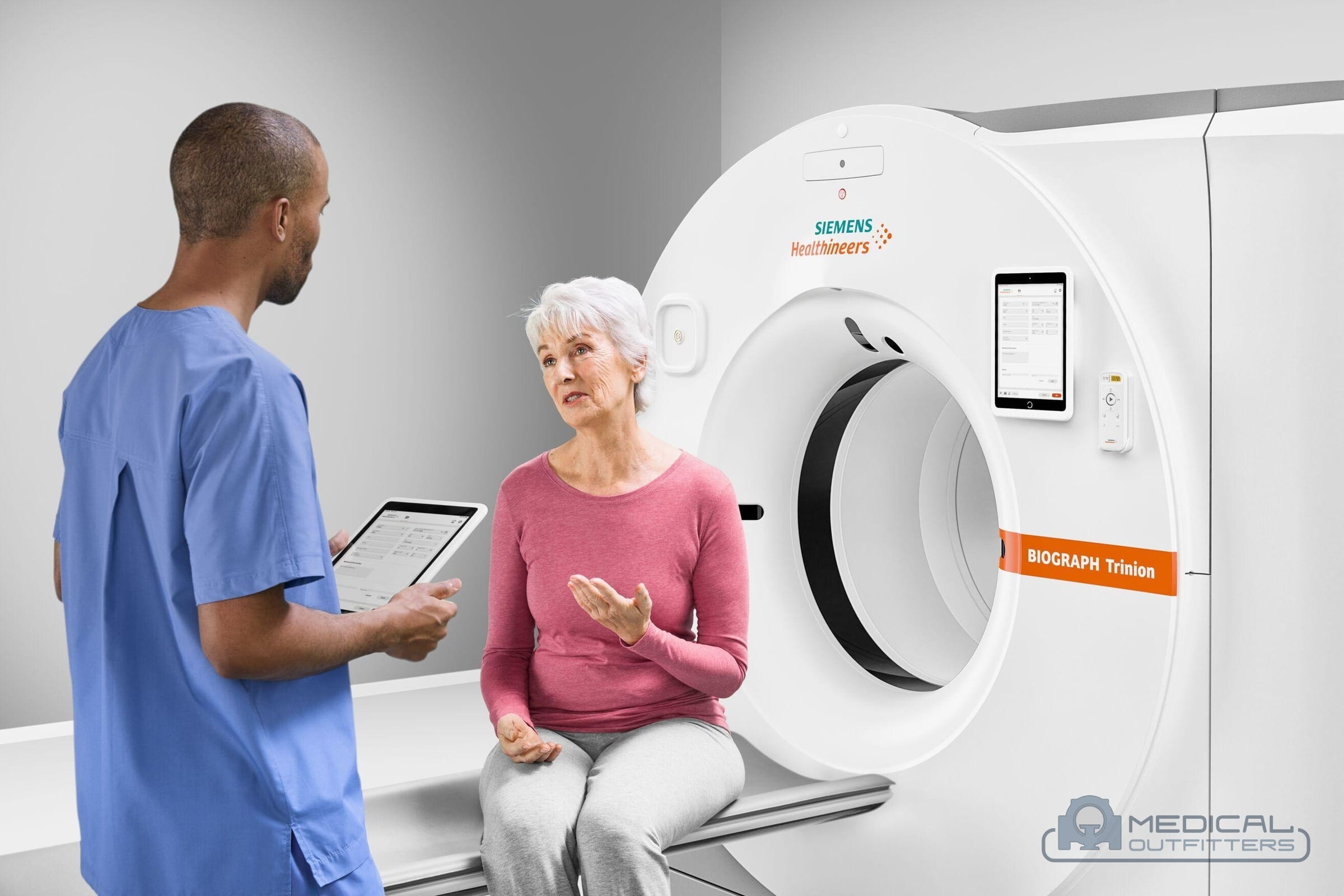 Technologist with a tablet talking with a seated patient beside a Siemens Biograph Trinion PET/CT scanner, photo courtesy of Siemens Healthineers, with the Medical Outfitters watermark