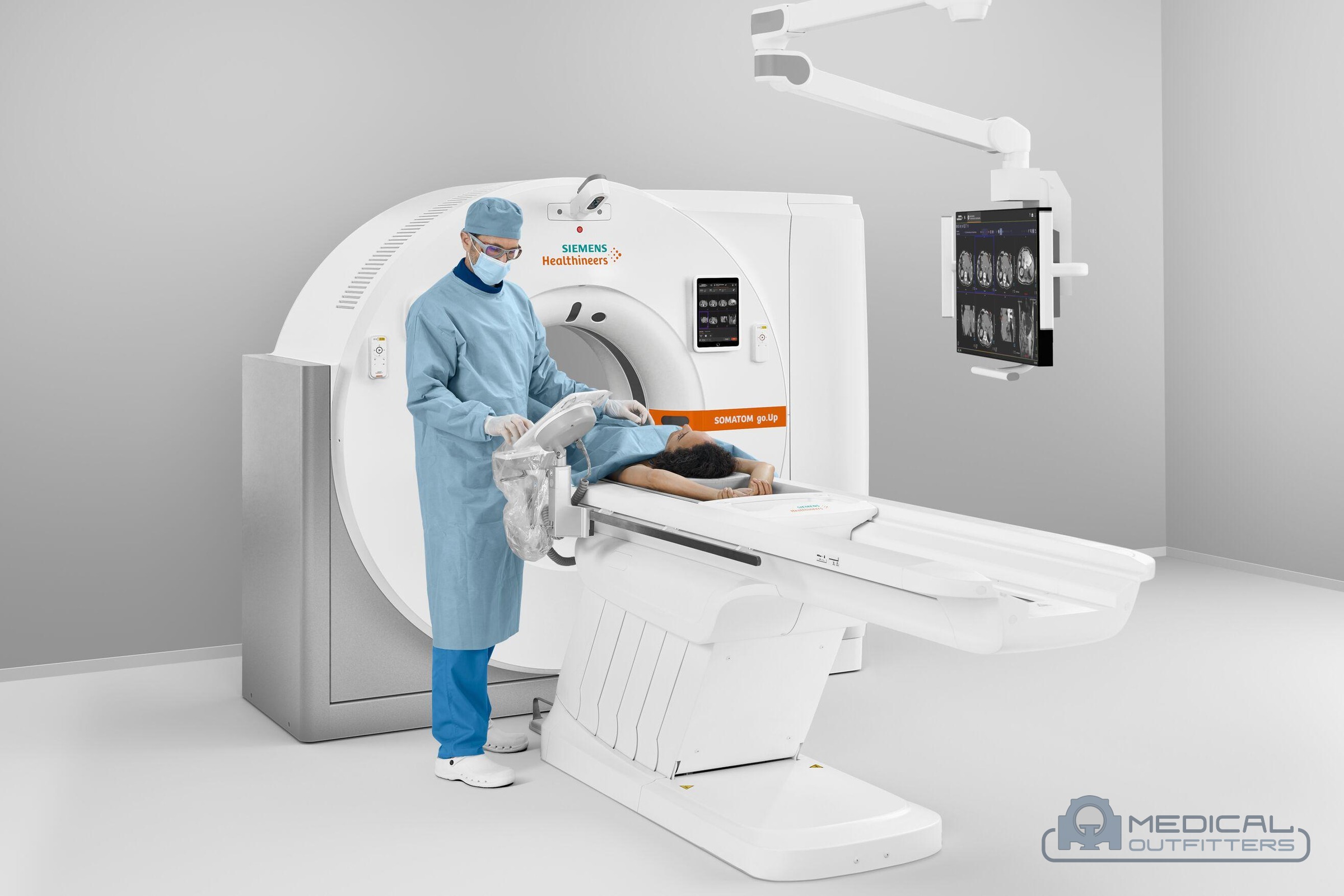 Clinician in sterile gown at the gantry of a Siemens SOMATOM go.Up CT scanner with a patient on the table and a ceiling-mounted monitor, photo courtesy of Siemens Healthineers