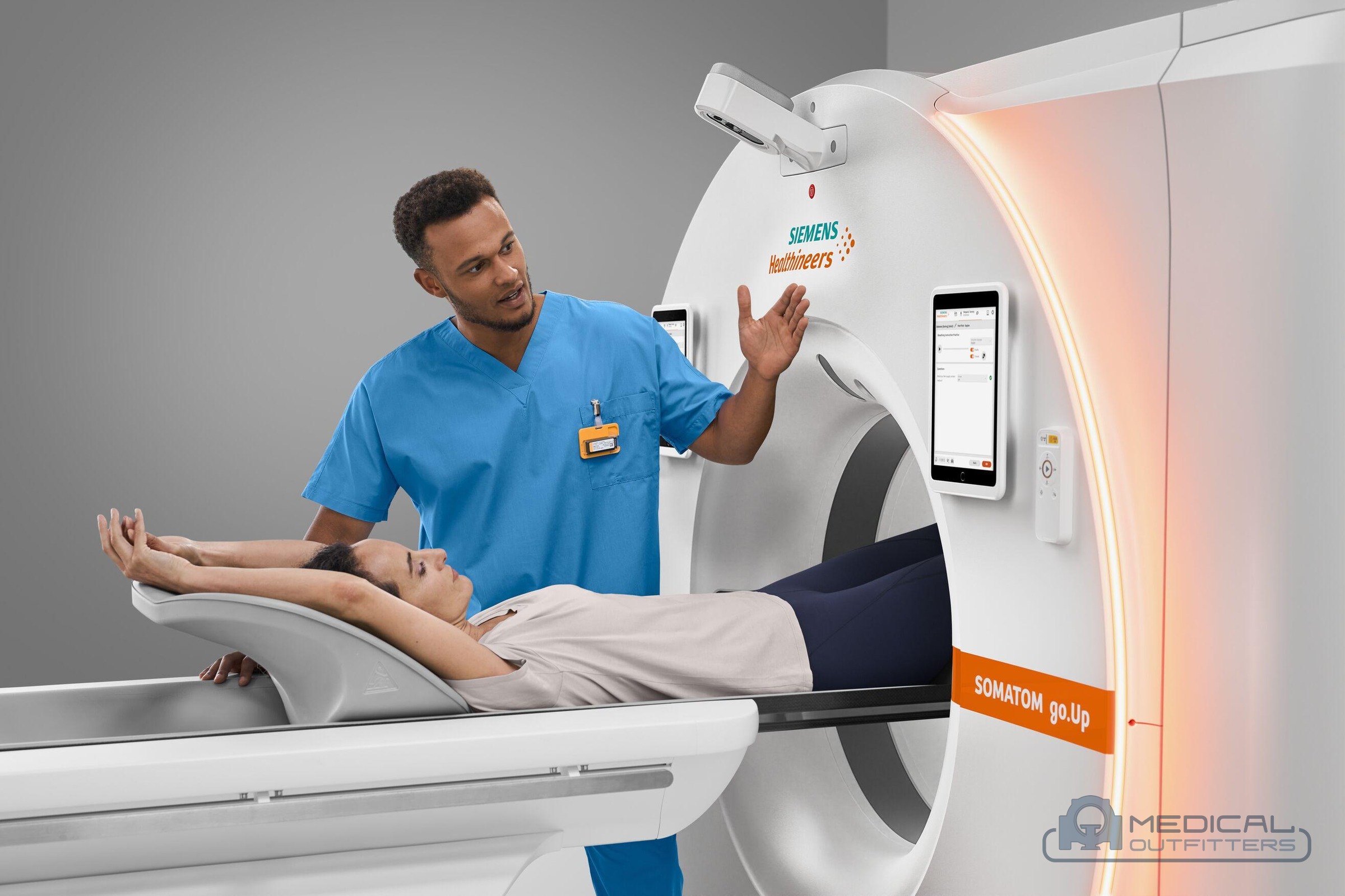 Technologist explaining the scan to a patient lying on the table of a Siemens SOMATOM go.Up CT scanner, photo courtesy of Siemens Healthineers, with the Medical Outfitters watermark