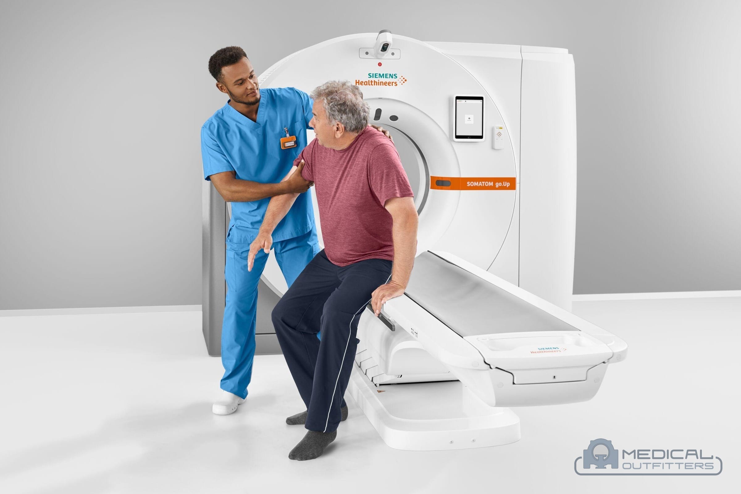Technologist helping a patient sit down on the table of a Siemens SOMATOM go.Up CT scanner, photo courtesy of Siemens Healthineers